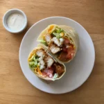 Overhead view of a crispy chicken wrap sliced open on a plate with ranch dipping sauce