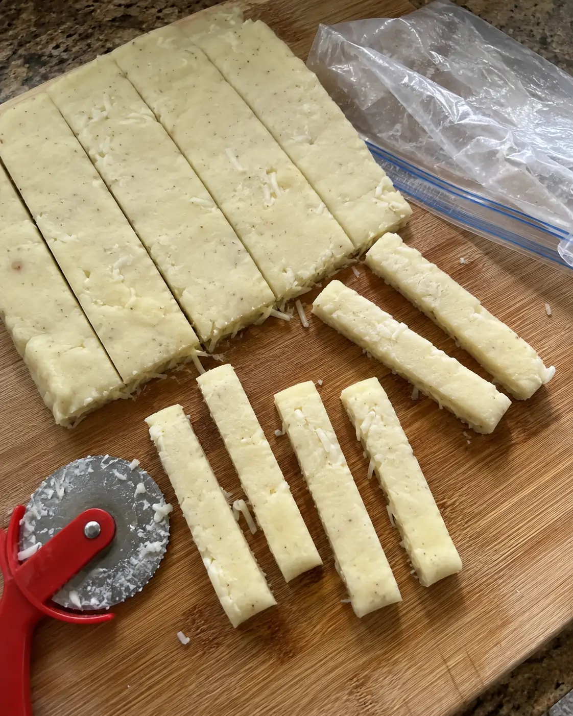 Chilled potato and mozzarella dough being cut into sticks with a pizza wheel on a cutting board