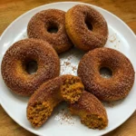 Cinnamon-sugar pumpkin donuts with one broken open to show the soft crumb