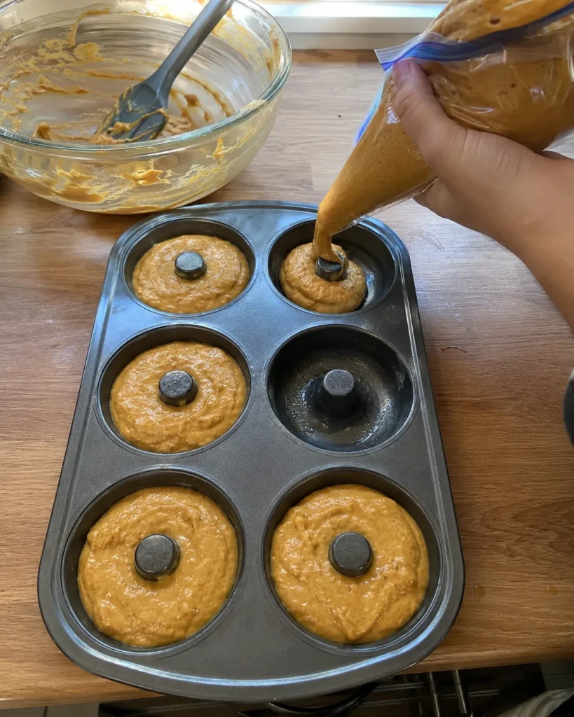 Pumpkin donut batter piped two-thirds full into a greased donut pan