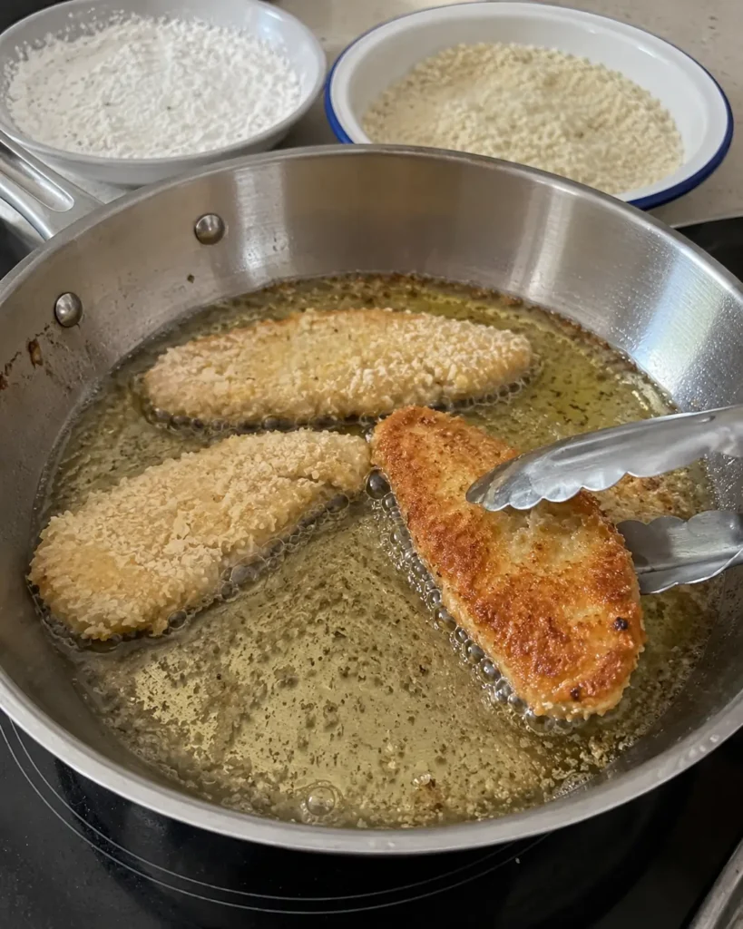 Panko-coated chicken strips frying in a skillet for crispy chicken wraps
