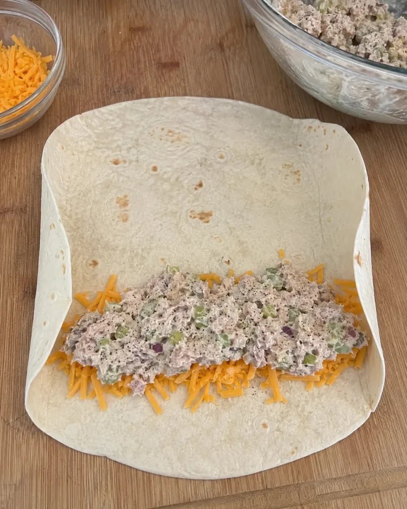 Folding a flour tortilla around tuna filling and shredded cheddar