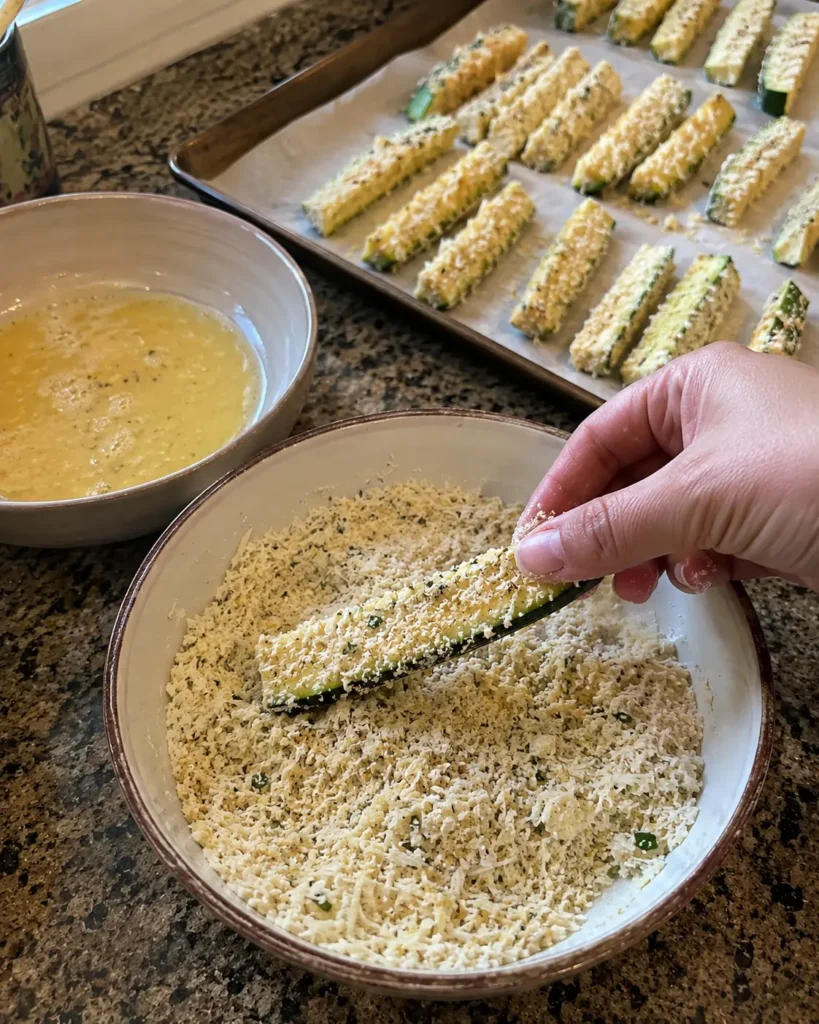 Coating a zucchini stick in almond flour and parmesan for Keto Zucchini Fries