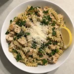 Overhead bowl of lemon parmesan chicken pasta salad with rotini, spinach, and a lemon wedge