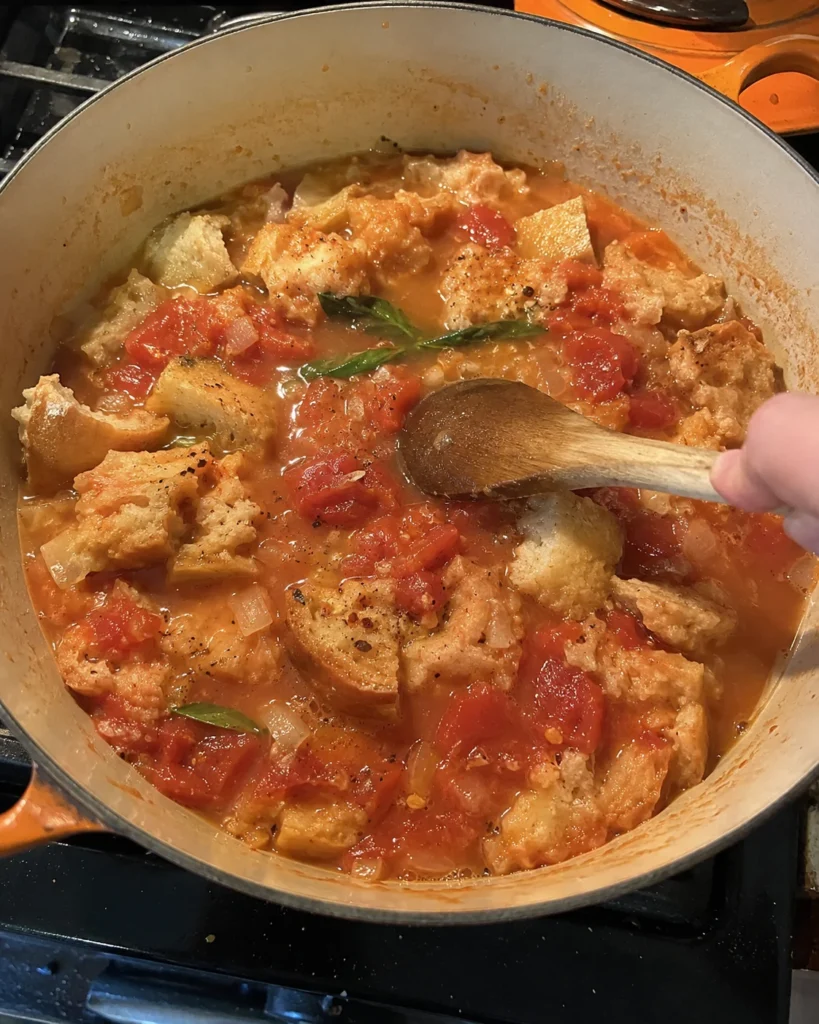 Torn rustic bread being stirred into tomato broth for Rustic Tomato and Bread Tuscan Soup Recipe