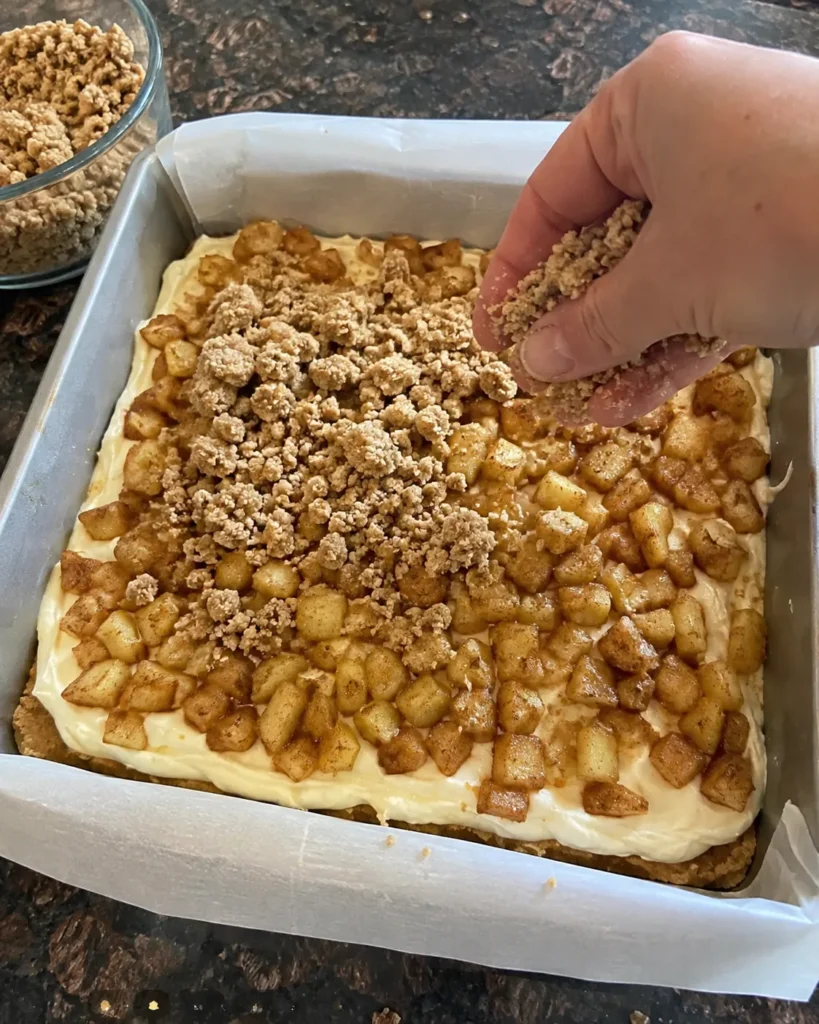 Adding streusel over apple pie cheesecake bars before baking
