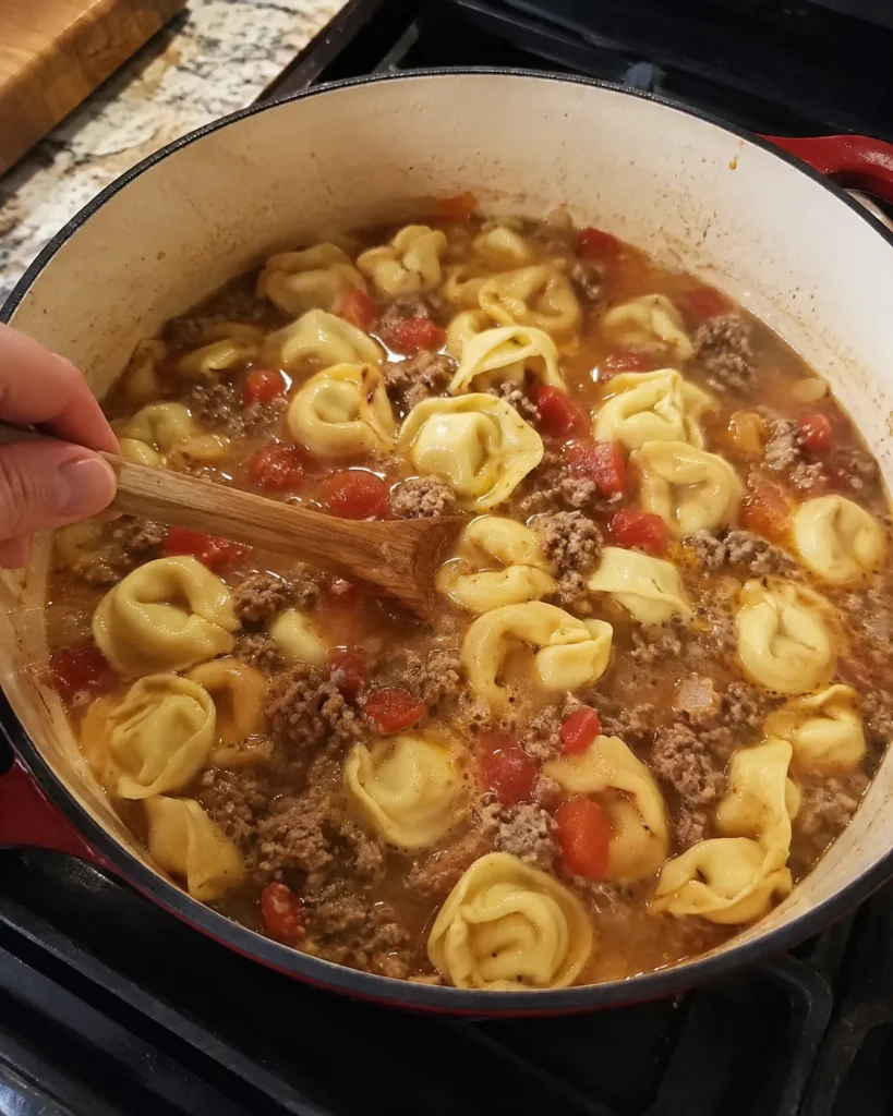 Cheese tortellini cooking with Italian sausage and tomatoes for Creamy Sausage Tortellini Soup