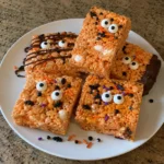 Five Halloween Rice Krispie treats arranged on a plate with candy eyes and chocolate