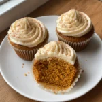 Three pumpkin cupcakes with cinnamon cream cheese frosting and a visible pumpkin-spice crumb