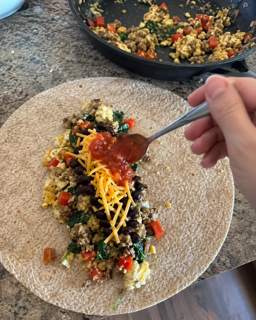 Assembling a High-Protein Breakfast Burrito with egg mixture, turkey sausage, black beans, cheddar, and salsa