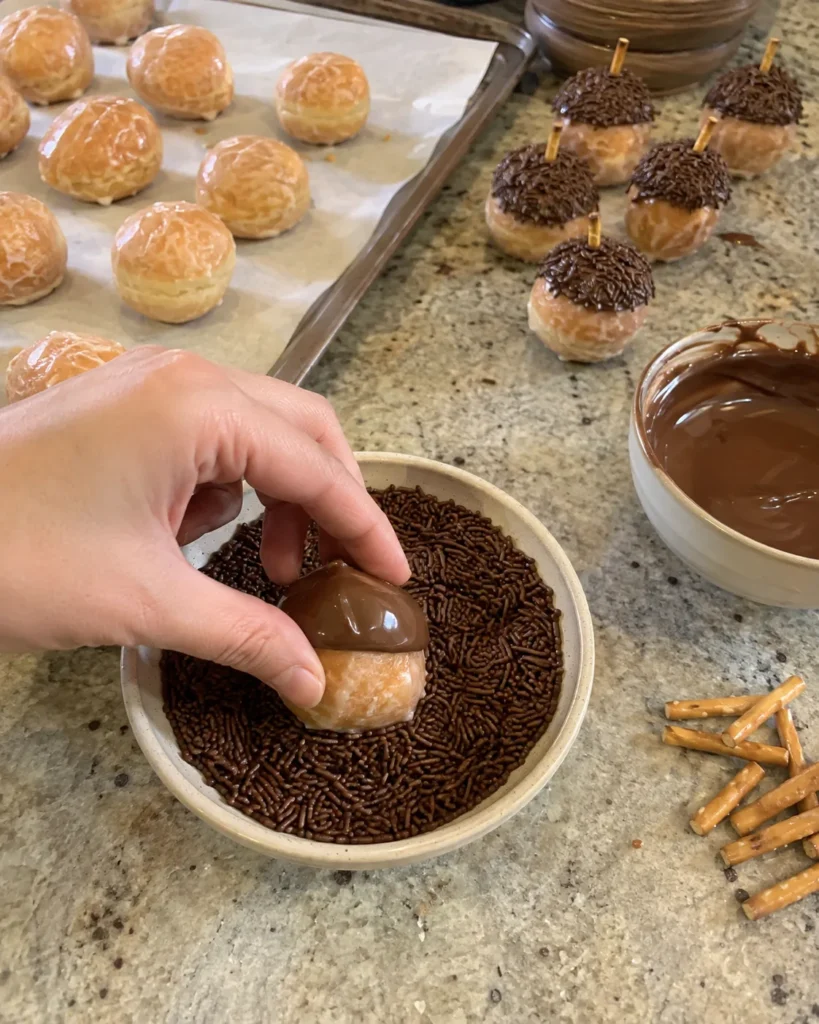 Glazed donut hole being dipped in chocolate jimmies while making Acorn Donut Holes