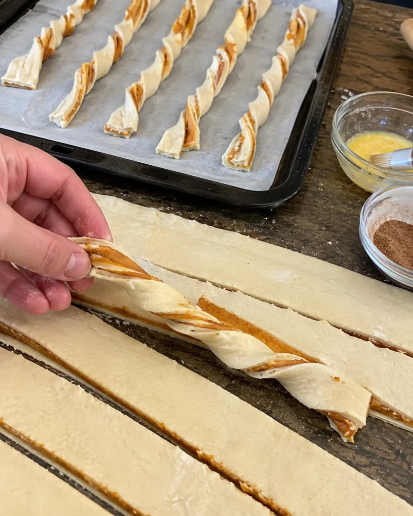 Hand twisting filled puff pastry strips while making Pumpkin Pie Twists