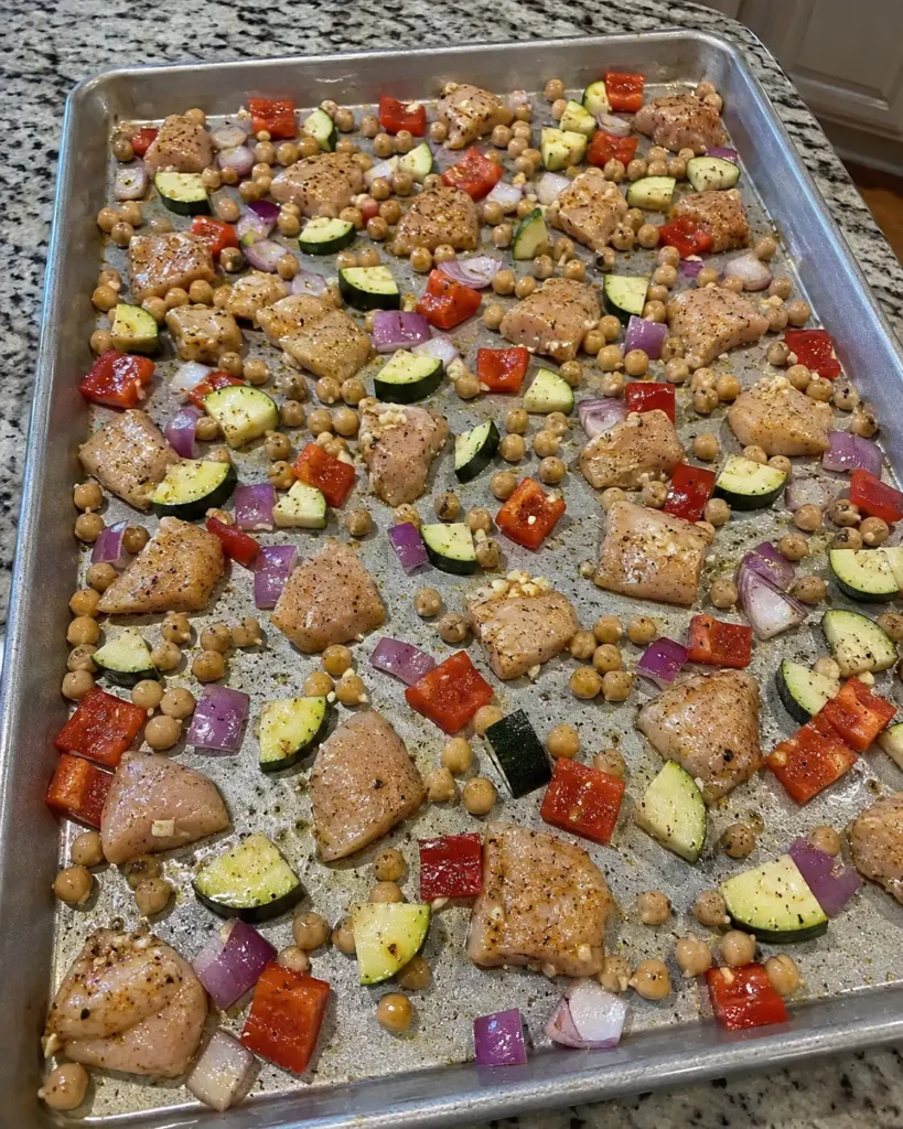 Chicken, chickpeas, zucchini, peppers, and onion spread on a sheet pan before roasting
