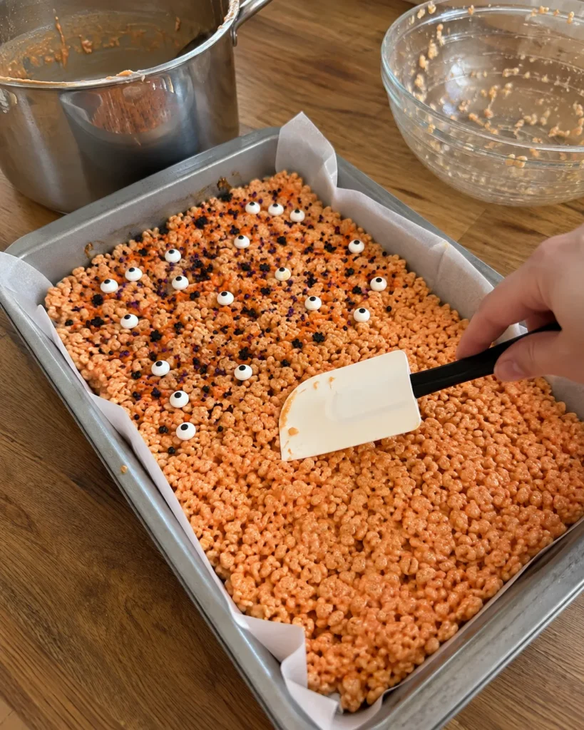 Halloween Rice Krispie treats mixture being pressed gently into a parchment-lined pan
