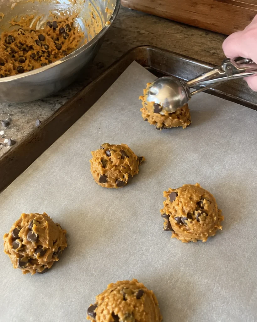 Pumpkin chocolate chip cookie dough being scooped onto a parchment-lined baking sheet